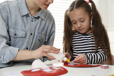 Woman and little girl making paper fly agaric at white table indoors, closeup. Child handmade craft