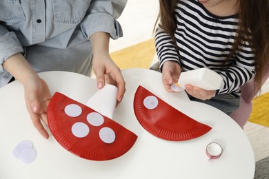 Woman and little girl making paper fly agarics at white table indoors, closeup. Child handmade craft