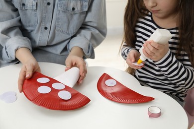 Woman and little girl making paper fly agarics at white table indoors, closeup. Child handmade craft