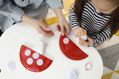 Photo of Woman and little girl making paper fly agarics at white table indoors, top view. Child handmade craft