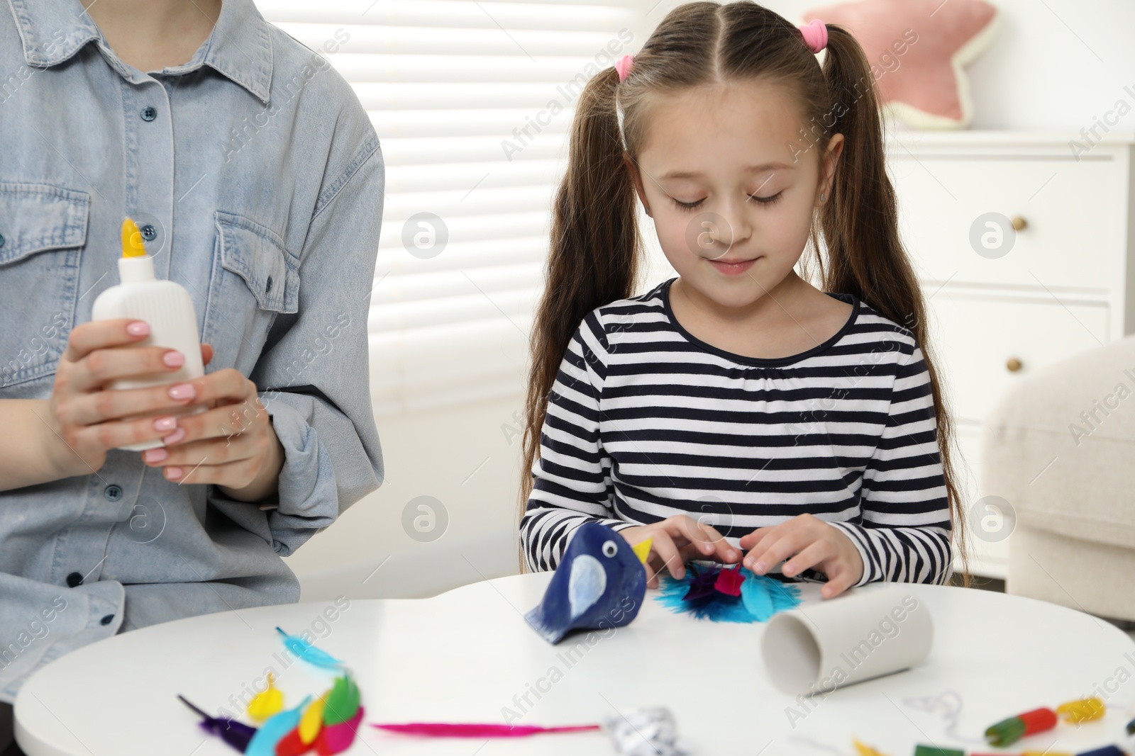 Photo of Woman and little girl making paper bird at white table indoors, closeup. Child handmade craft