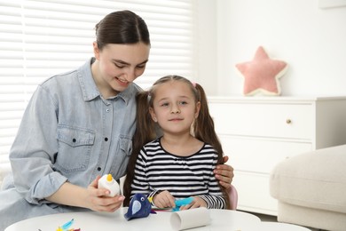 Woman and little girl making paper bird at white table indoors. Child handmade craft