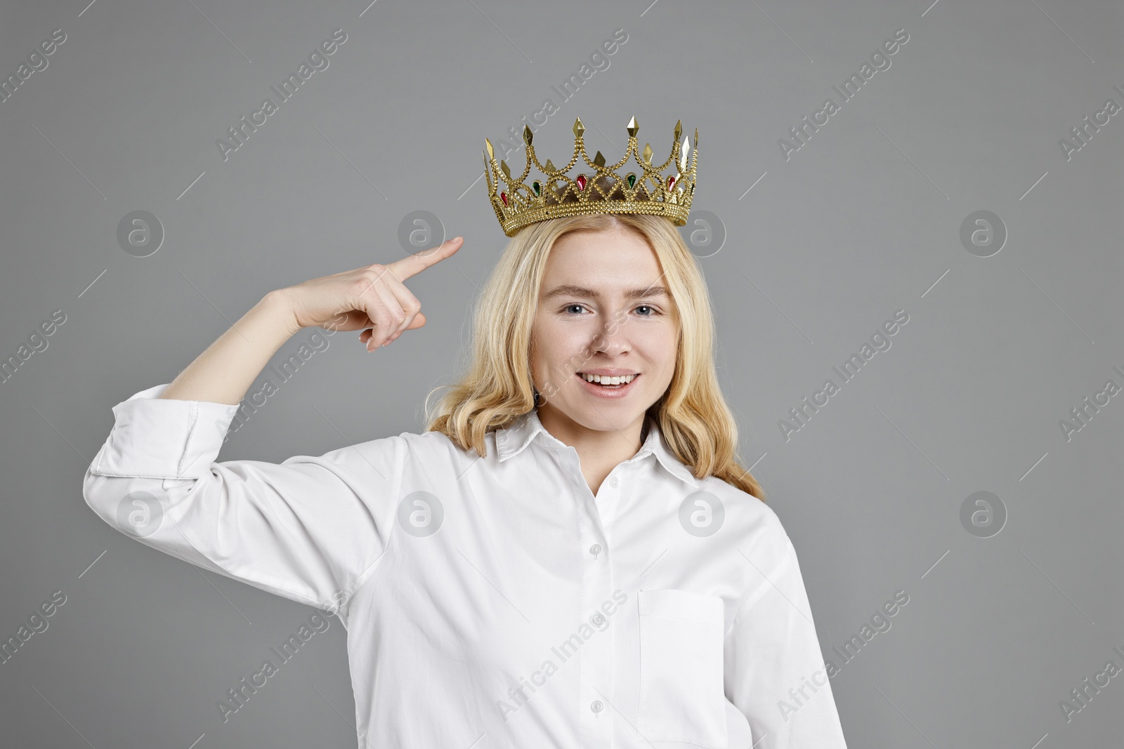 Photo of Happy woman pointing at elegant crown on grey background