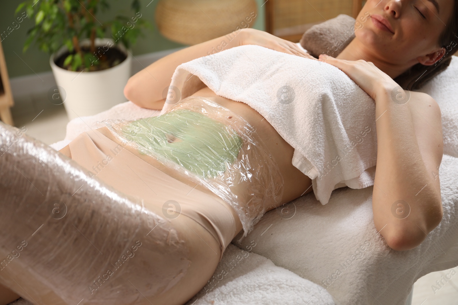 Photo of Woman undergoing body wraps treatment in spa salon, closeup