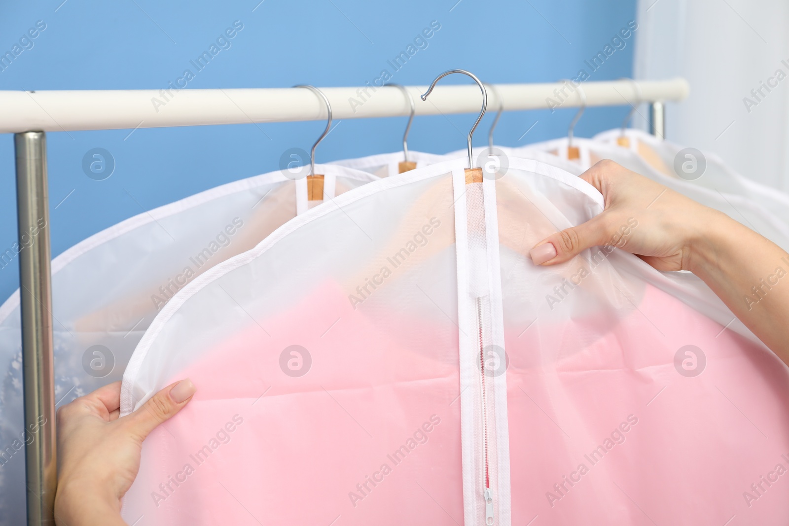 Photo of Woman taking garment cover with clothes from rack indoors, closeup