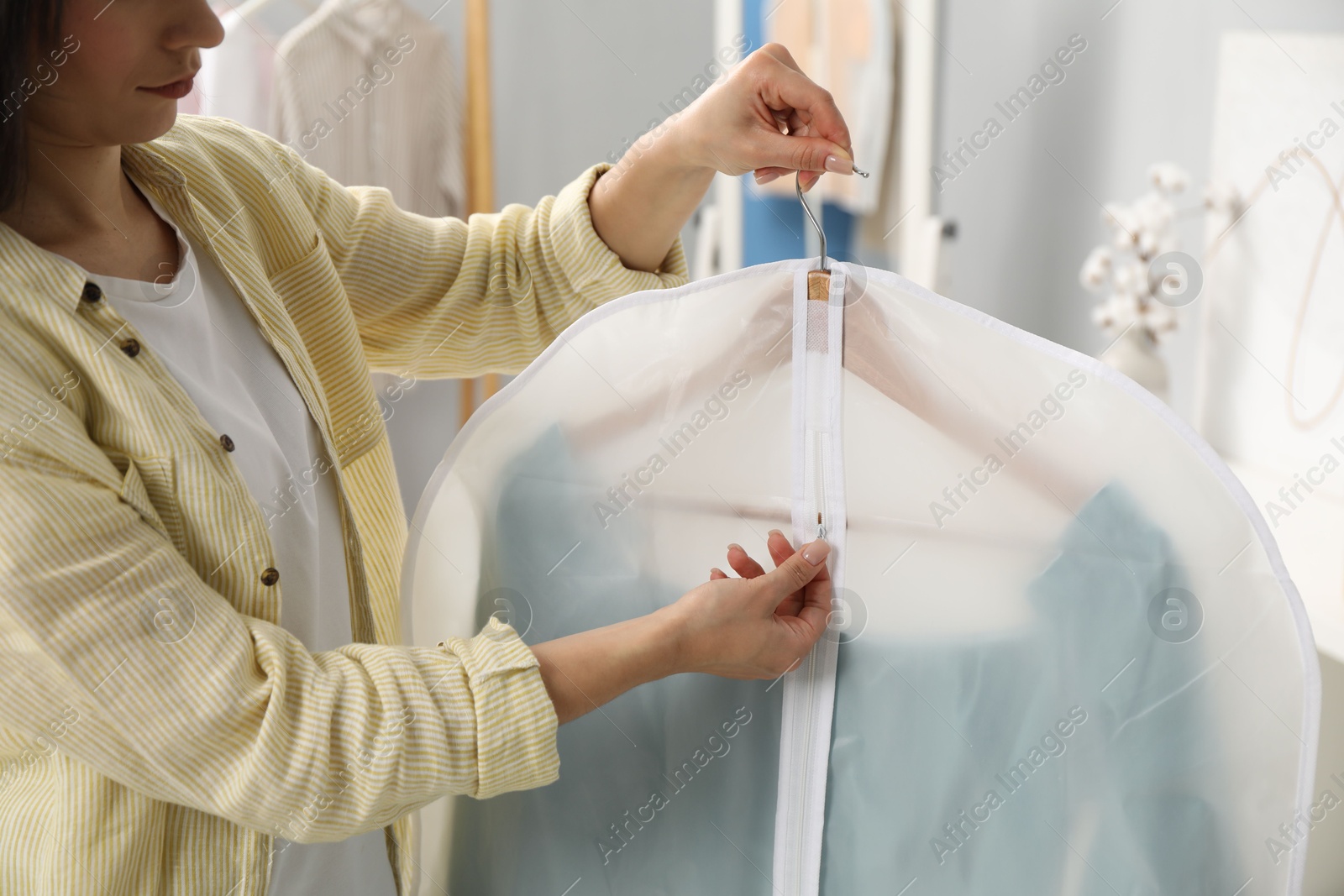 Photo of Woman zipping garment cover with clothes indoors, closeup