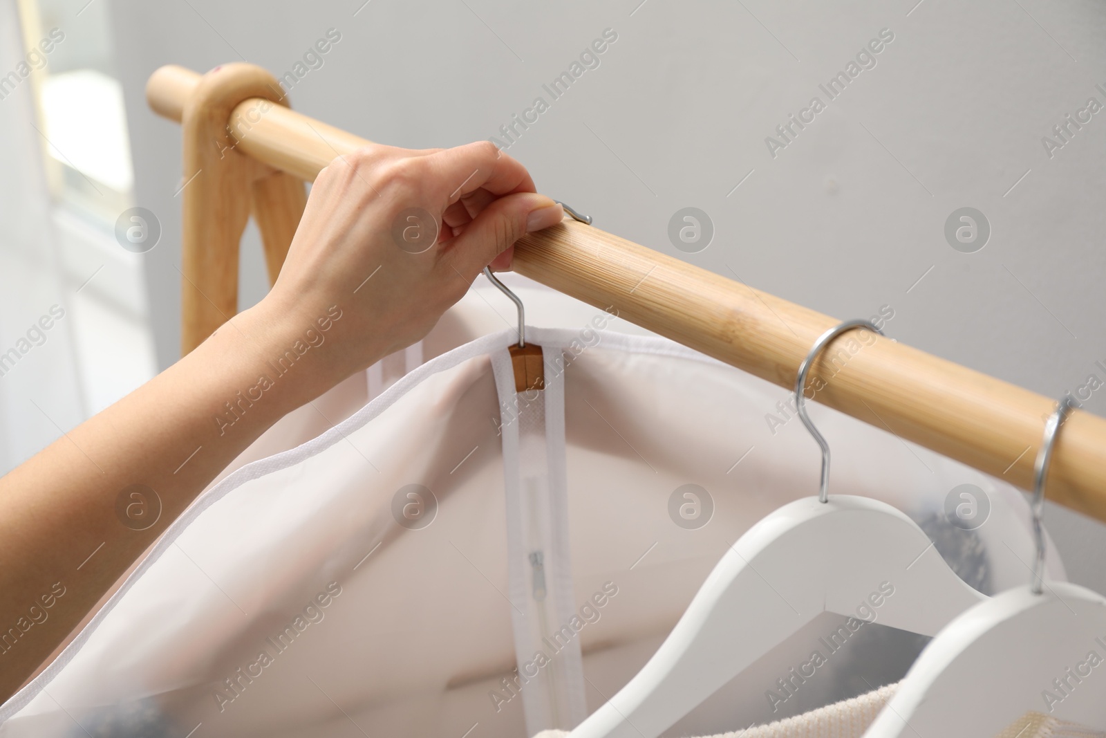 Photo of Woman taking garment cover with clothes from rack indoors, closeup