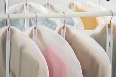 Photo of Garment covers with clothes on rack indoors, closeup