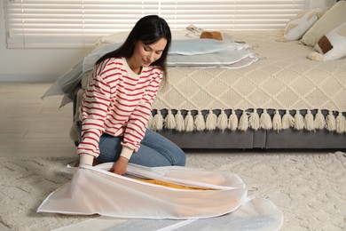 Woman putting clothes into garment cover on floor indoors