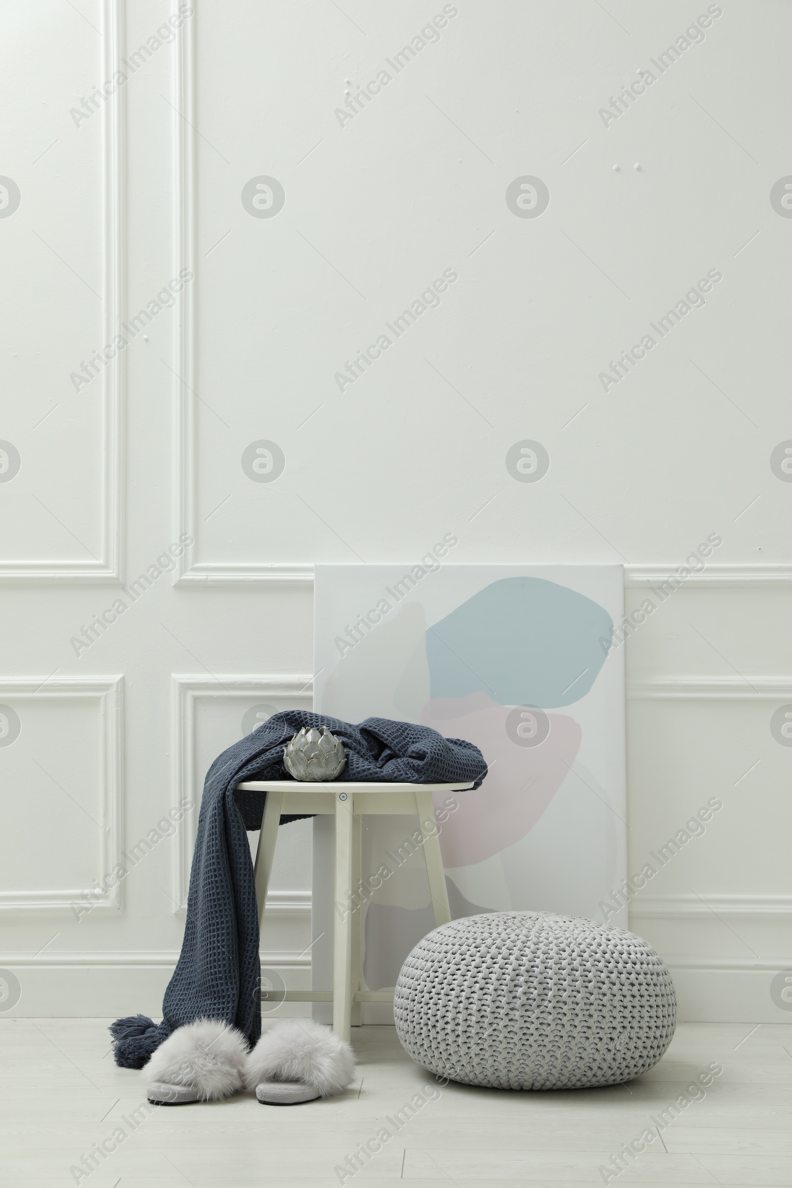 Photo of Knitted pouf, fuzzy slippers and decor elements near white wall indoors. Space for text