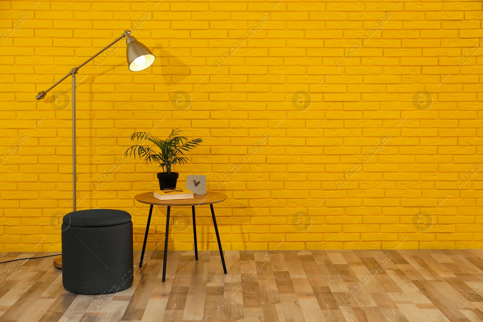 Photo of Stylish black pouf, lamp and table near yellow brick wall in room. Space for text