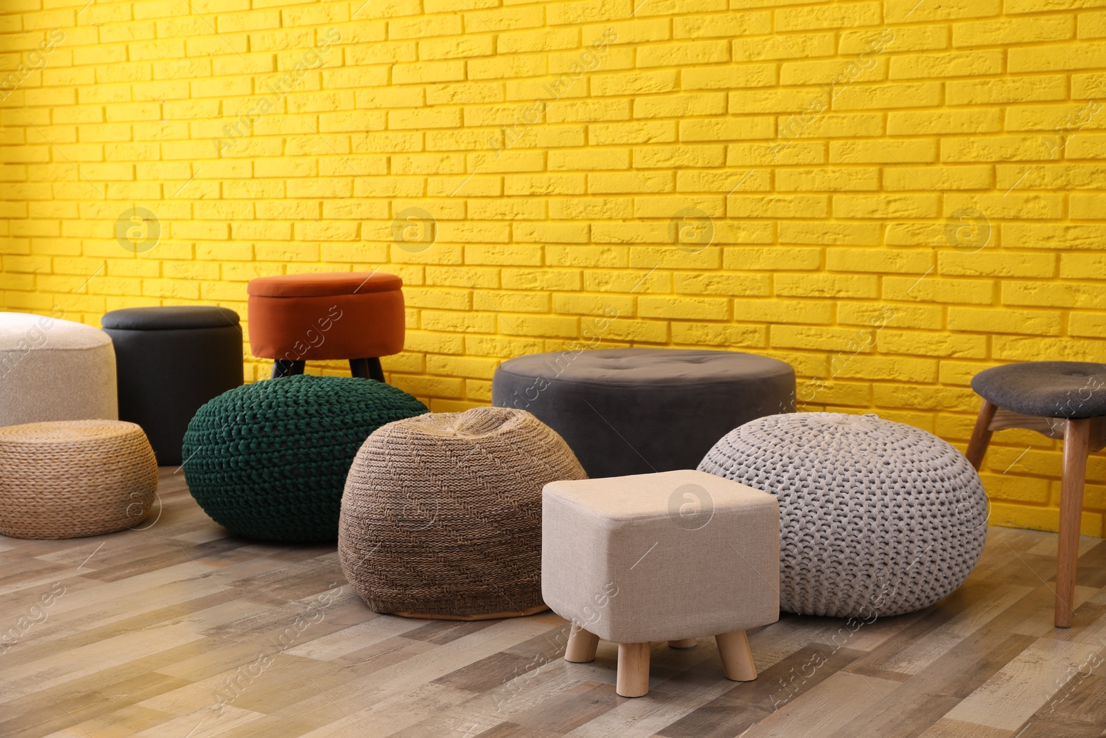 Photo of Different stylish poufs and ottomans near yellow brick wall