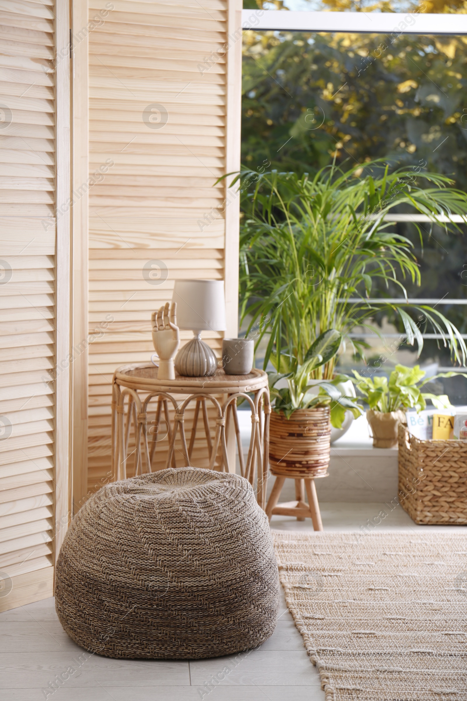 Photo of Stylish knitted pouf, wicker furniture and beautiful houseplants in room. Interior design