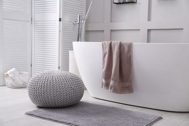 Photo of Stylish knitted pouf on floor in modern bathroom. Interior design