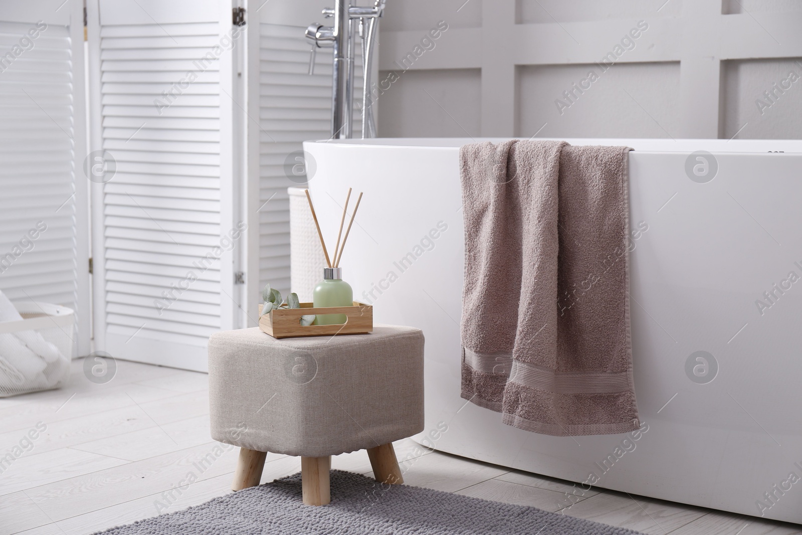 Photo of Stylish ottoman with air reed freshener on floor in modern bathroom. Interior design