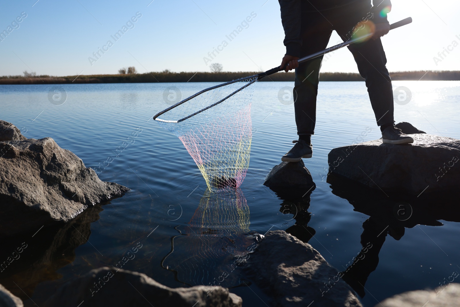 Photo of Fisherman holding fishing net with catch at riverside, closeup