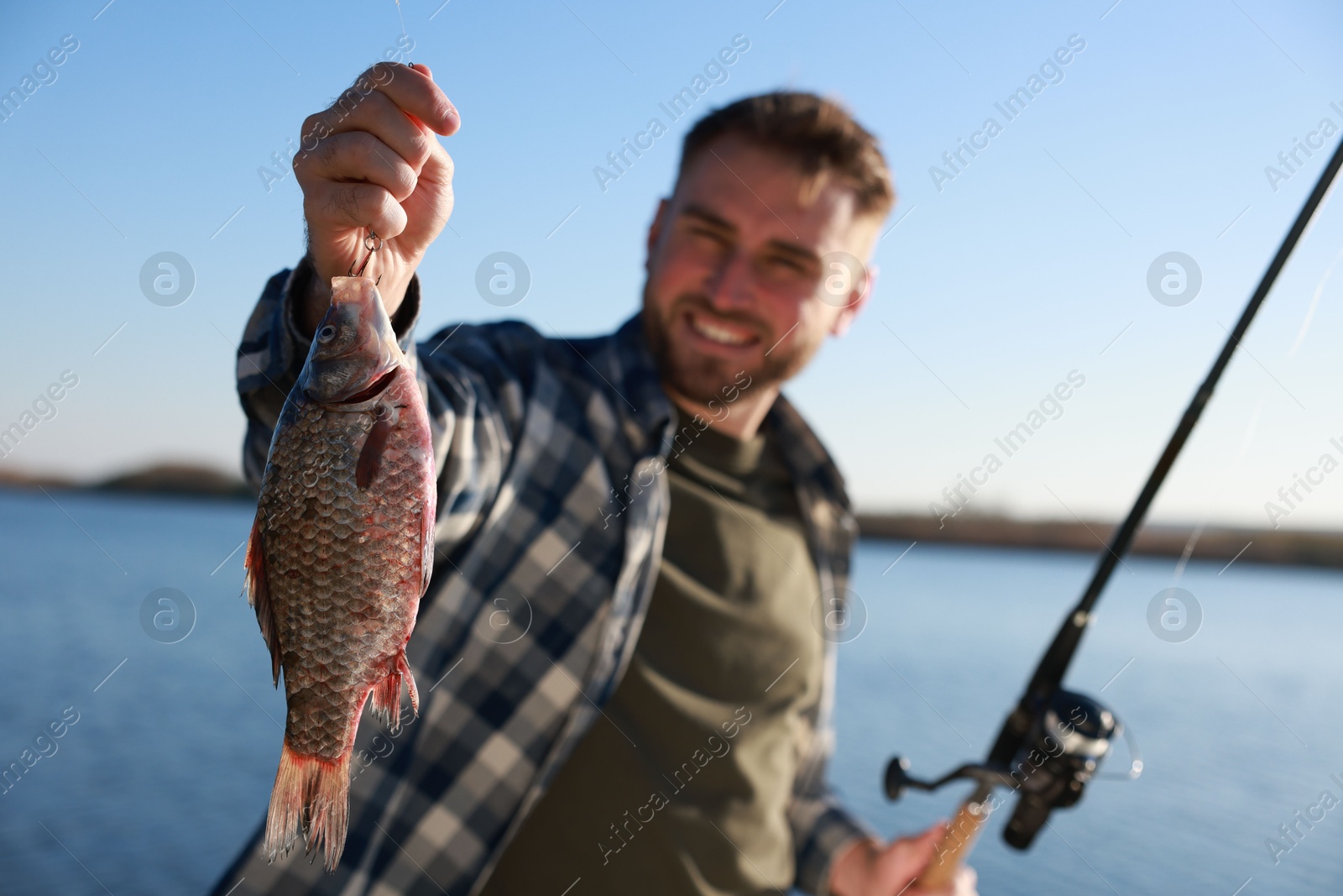 Photo of Fisherman with fishing rod at riverside, focus on catch