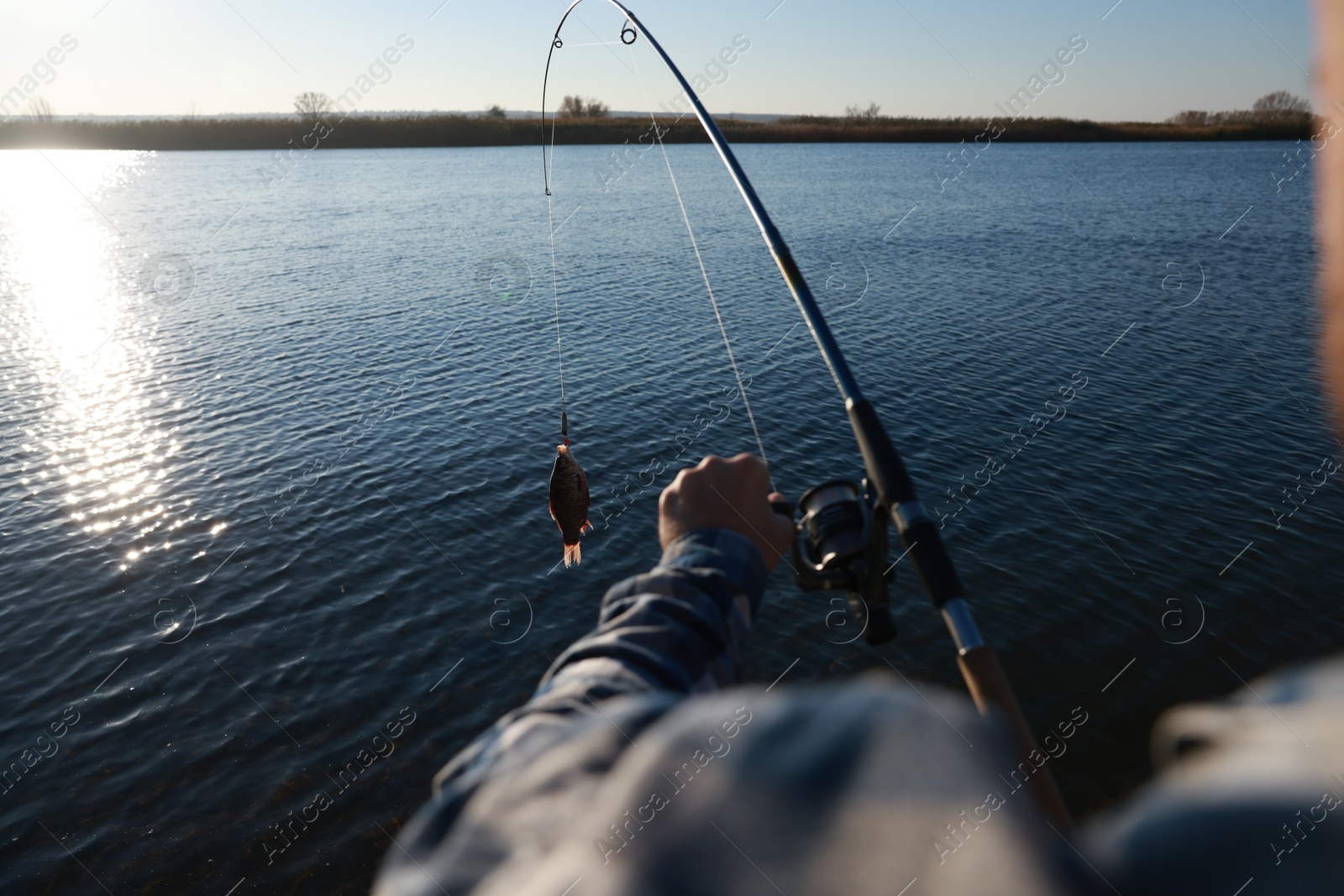 Photo of Fisherman catching fish with rod at riverside, closeup