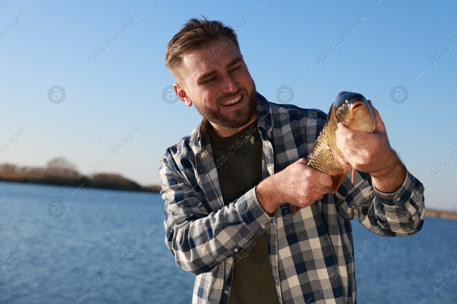 Photo of Fisherman holding caught fish at riverside. Recreational activity