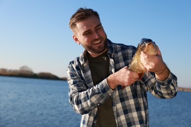 Photo of Fisherman holding caught fish at riverside. Recreational activity