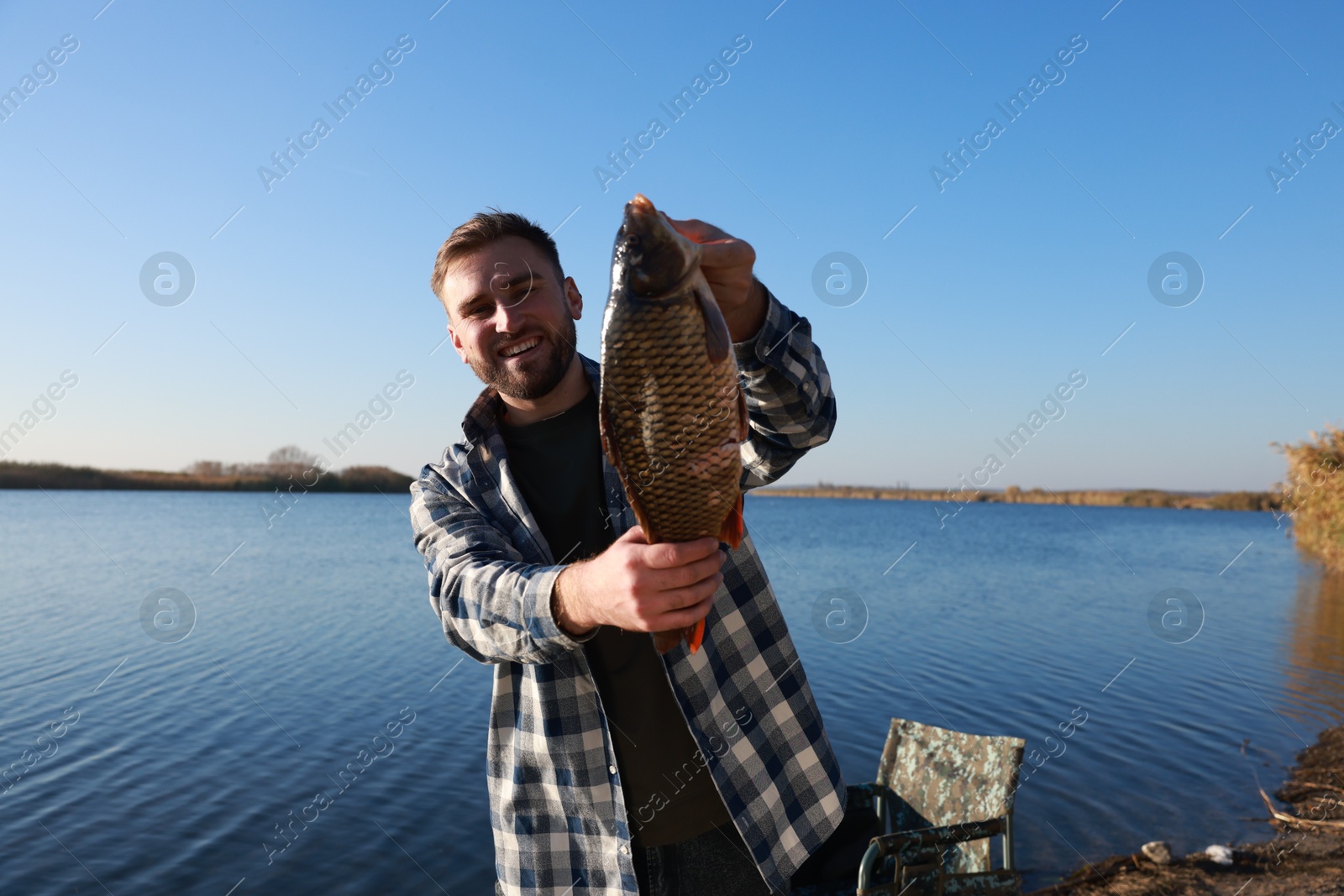 Photo of Fisherman holding caught fish at riverside. Recreational activity