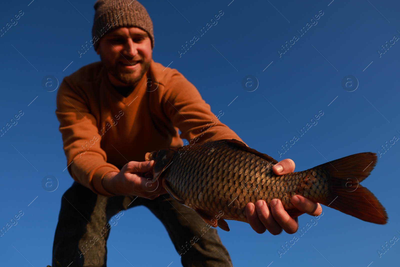 Photo of Fisherman holding caught fish against blue sky, low angle view