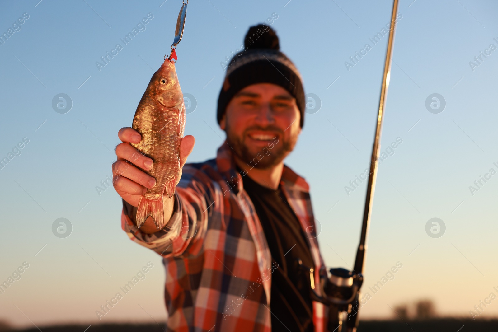 Photo of Fisherman with rod and catch at riverside, focus on fish