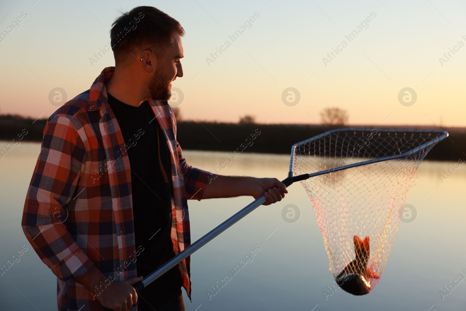 Photo of Fisherman holding fishing net with catch at riverside