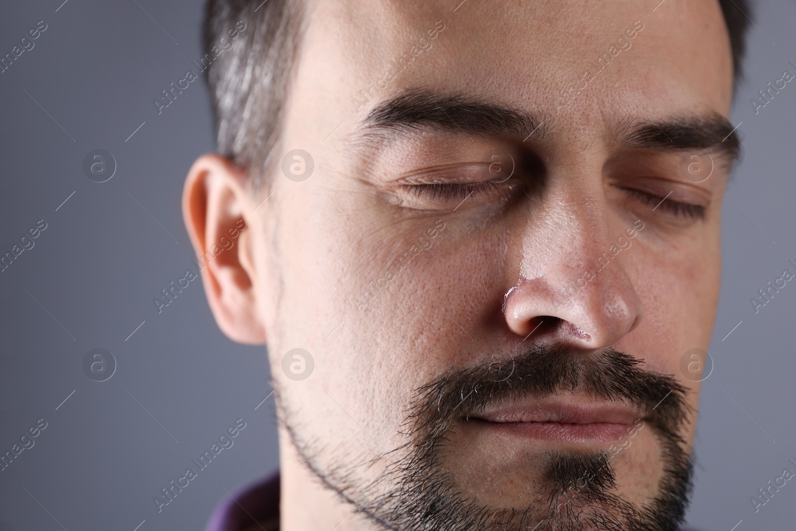 Photo of Sad man crying on grey background, closeup