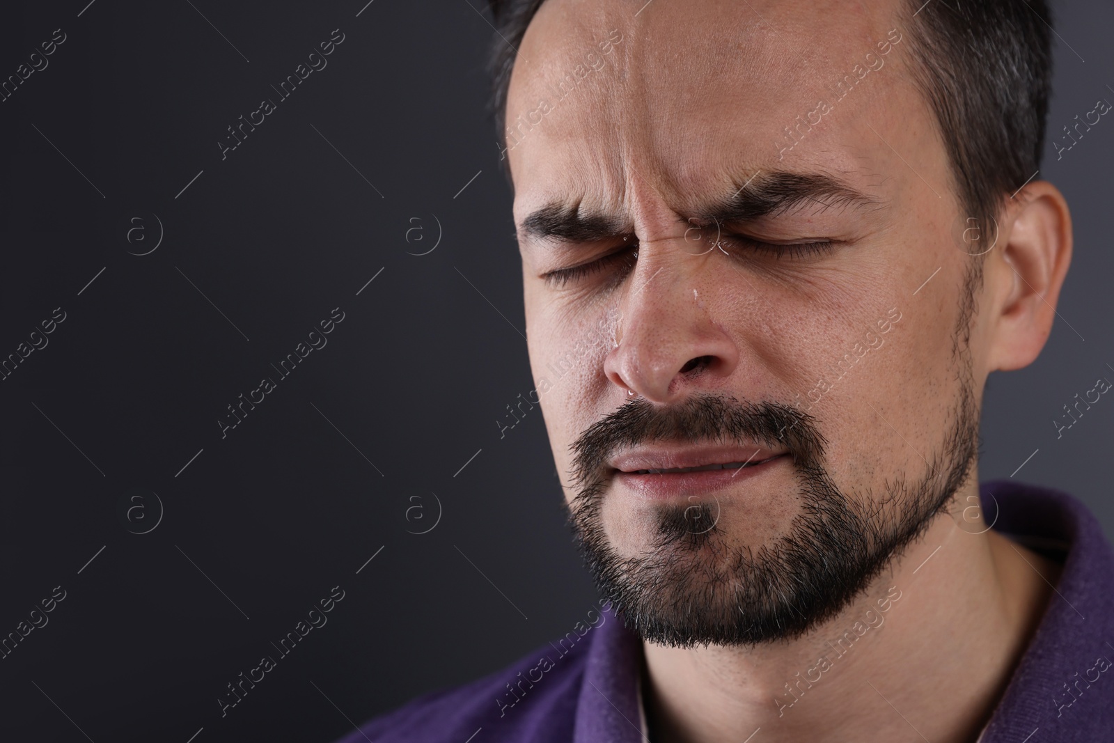 Photo of Sad man crying on grey background, closeup. Space for text