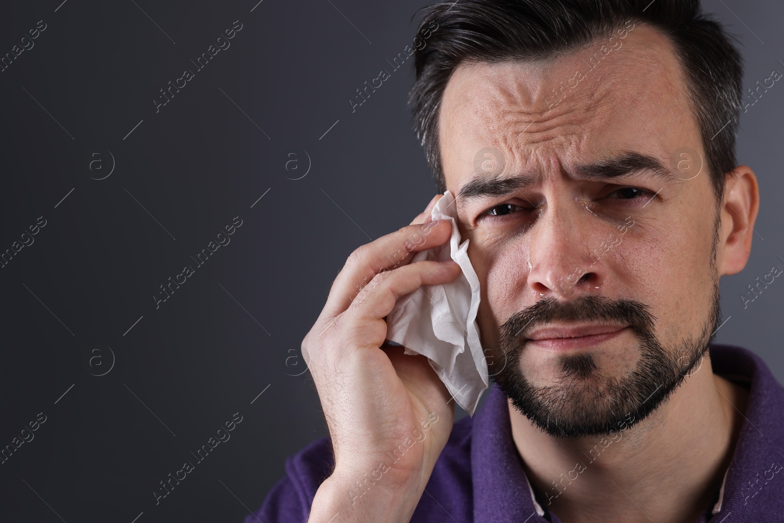 Photo of Sad man with paper tissue crying on grey background, space for text