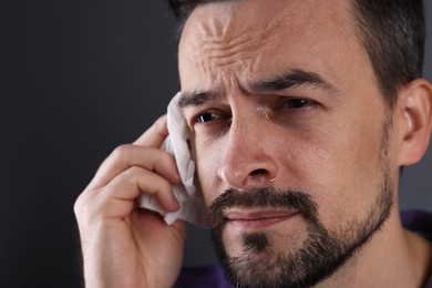 Sad man with paper tissue crying on grey background, closeup