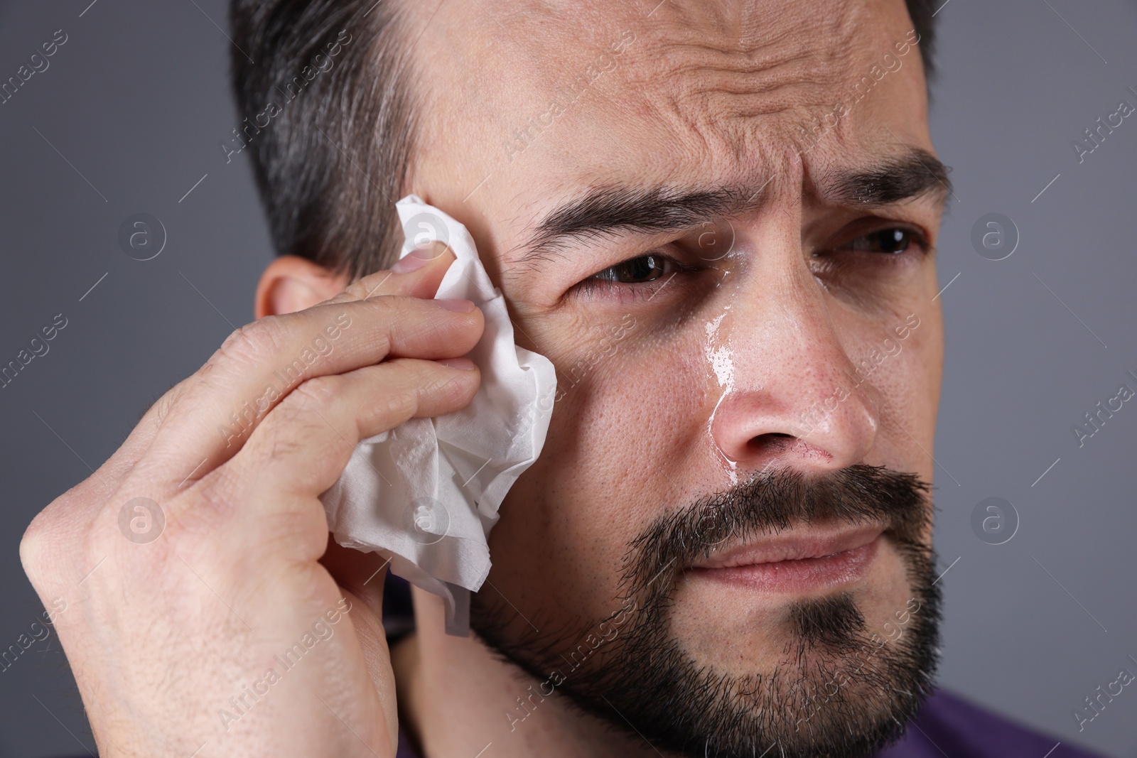 Photo of Sad man with paper tissue crying on grey background, closeup