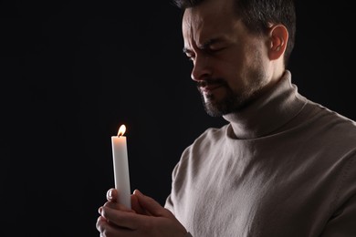 Photo of Sad man with burning candle crying on black background, space for text