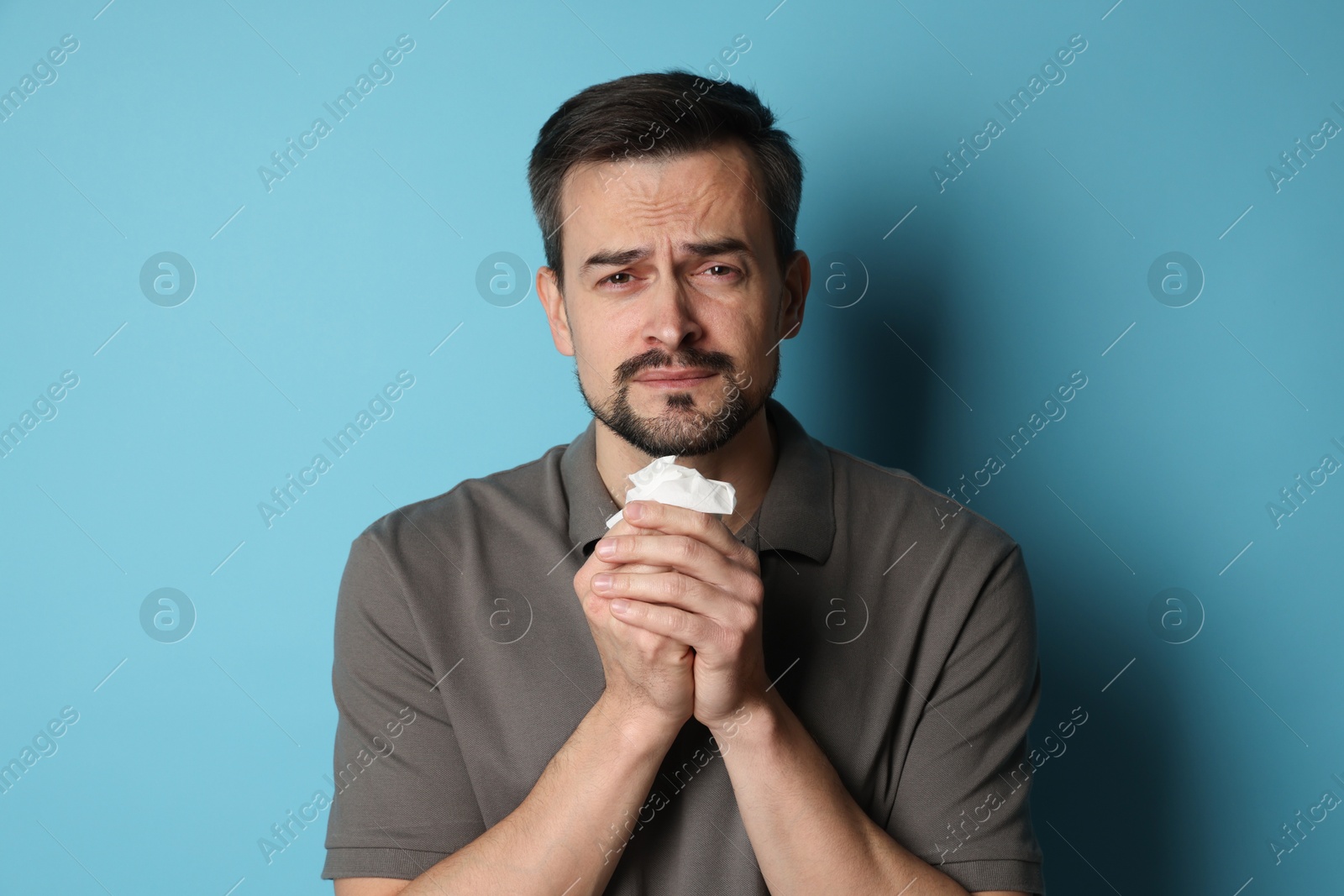 Photo of Sad man with paper tissue crying on light blue background