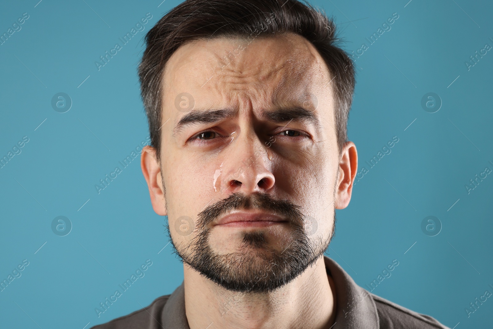 Photo of Sad man crying on light blue background, closeup