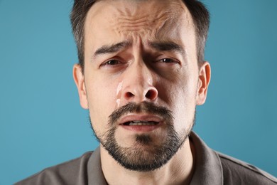 Sad man crying on light blue background, closeup