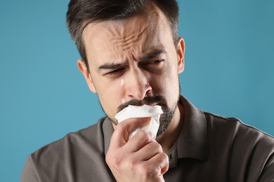 Photo of Sad man with paper tissue crying on light blue background