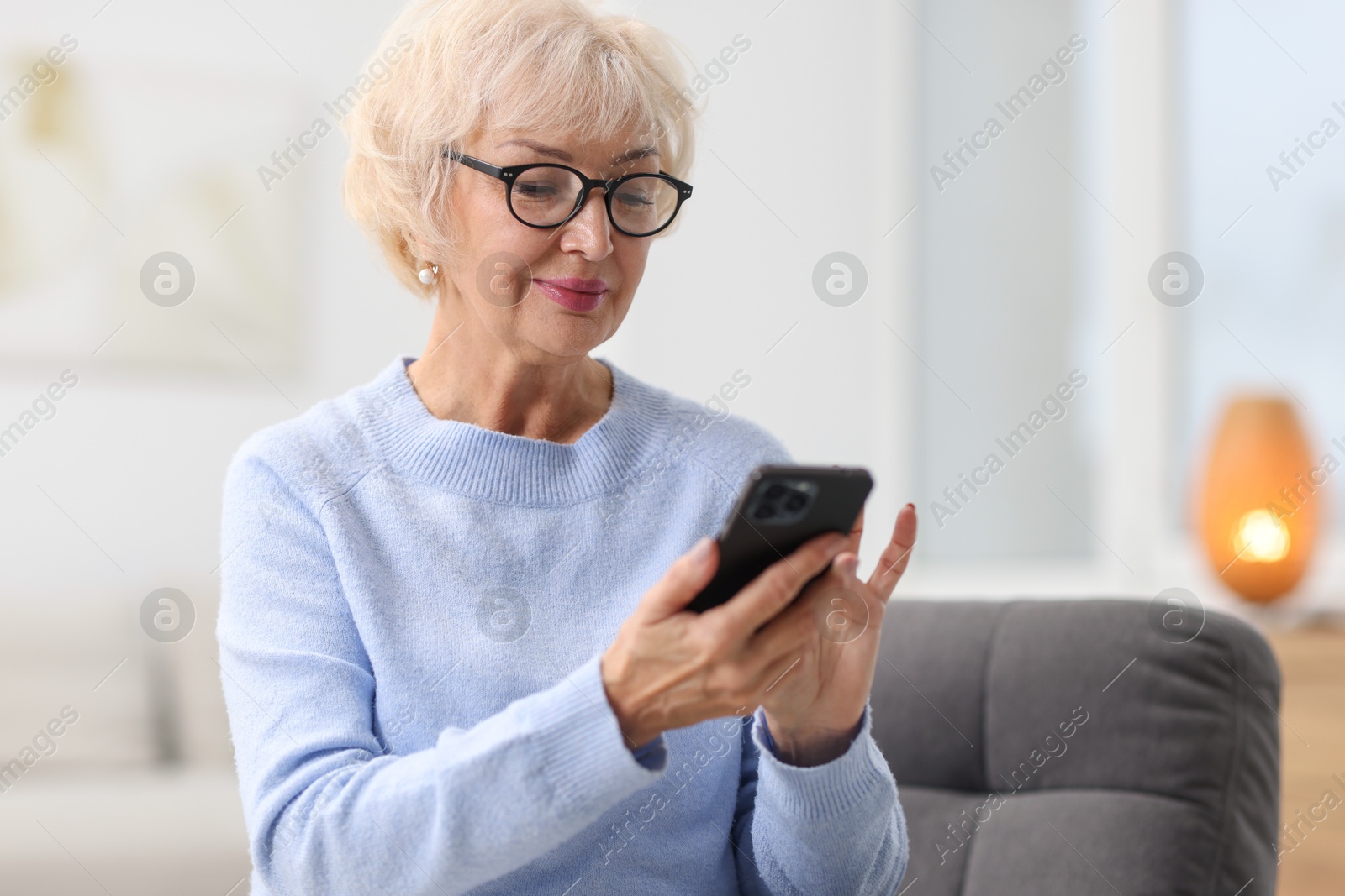 Photo of Beautiful grandmother using smartphone at home. Space for text