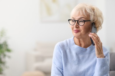 Photo of Beautiful grandmother talking on smartphone at home. Space for text