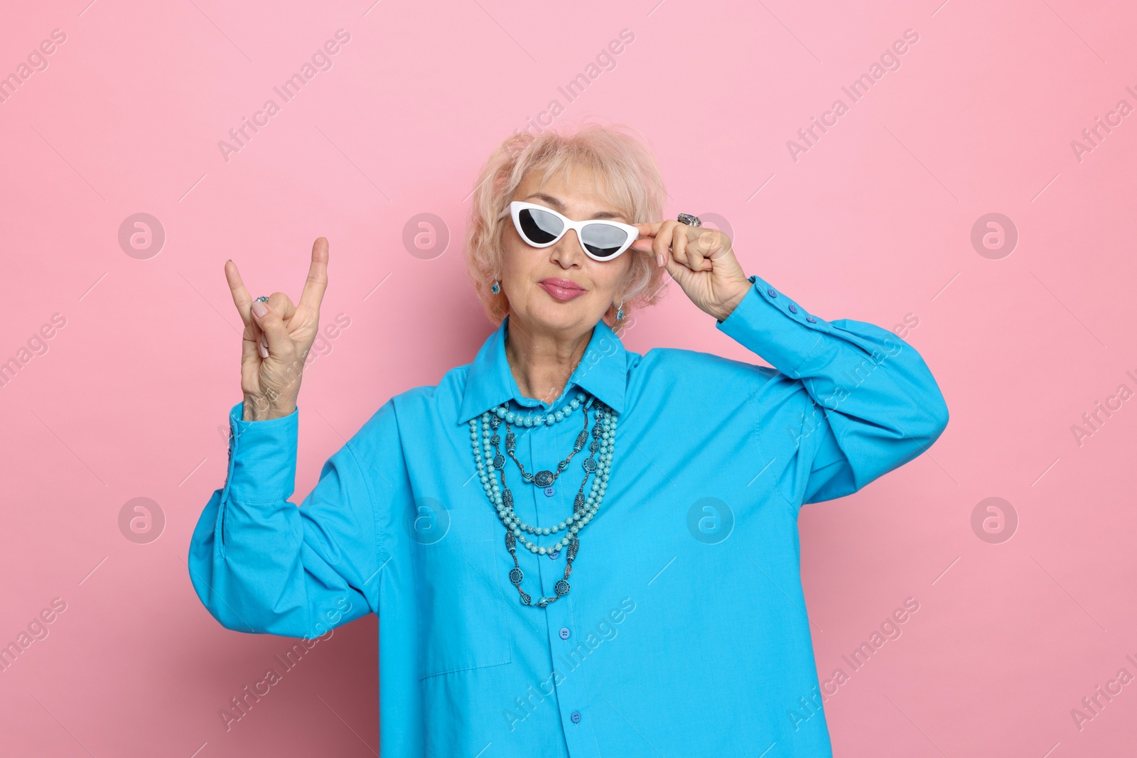 Photo of Cool grandmother showing rock gesture on pink background