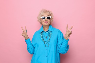 Photo of Cool grandmother showing V-signs on pink background