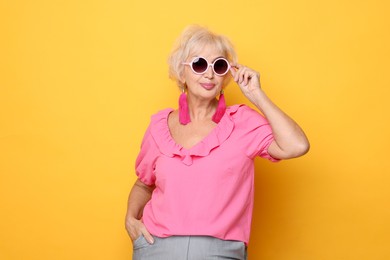 Photo of Portrait of fashionable grandmother in sunglasses on orange background