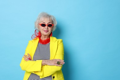 Photo of Portrait of fashionable grandmother in sunglasses and yellow jacket on light blue background. Space for text