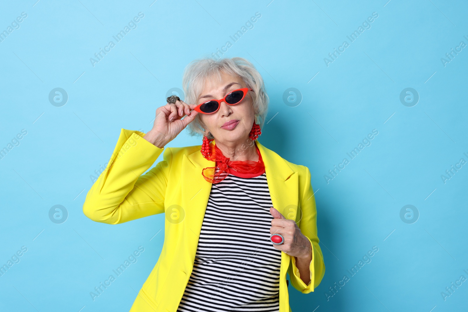 Photo of Portrait of fashionable grandmother in sunglasses and yellow jacket on light blue background