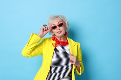 Portrait of fashionable grandmother in sunglasses and yellow jacket on light blue background