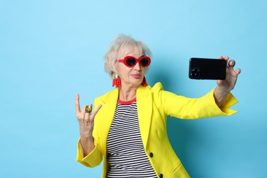 Photo of Cool grandmother showing rock gesture while taking selfie on light blue background