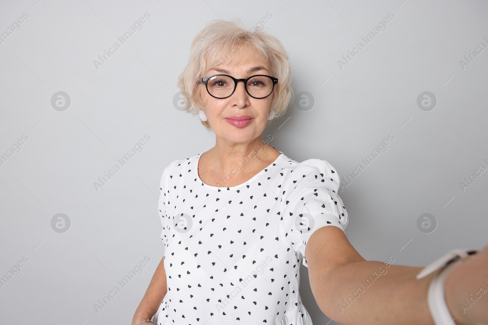 Photo of Elegant grandmother taking selfie on light grey background