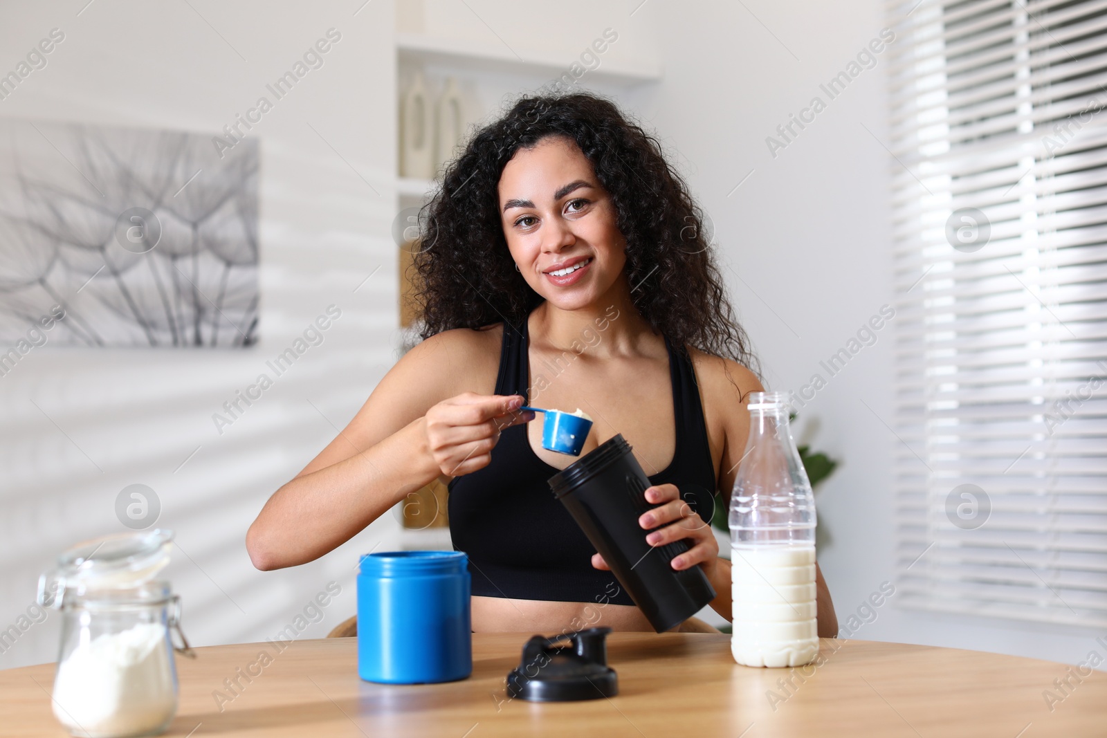 Photo of Beautiful woman making protein shake at wooden table indoors