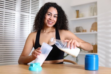 Photo of Beautiful woman making protein shake at wooden table indoors